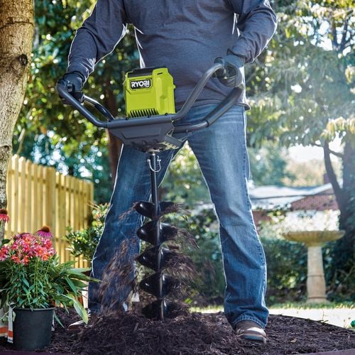 A person operating a hole digger to dig a hole in a garden.