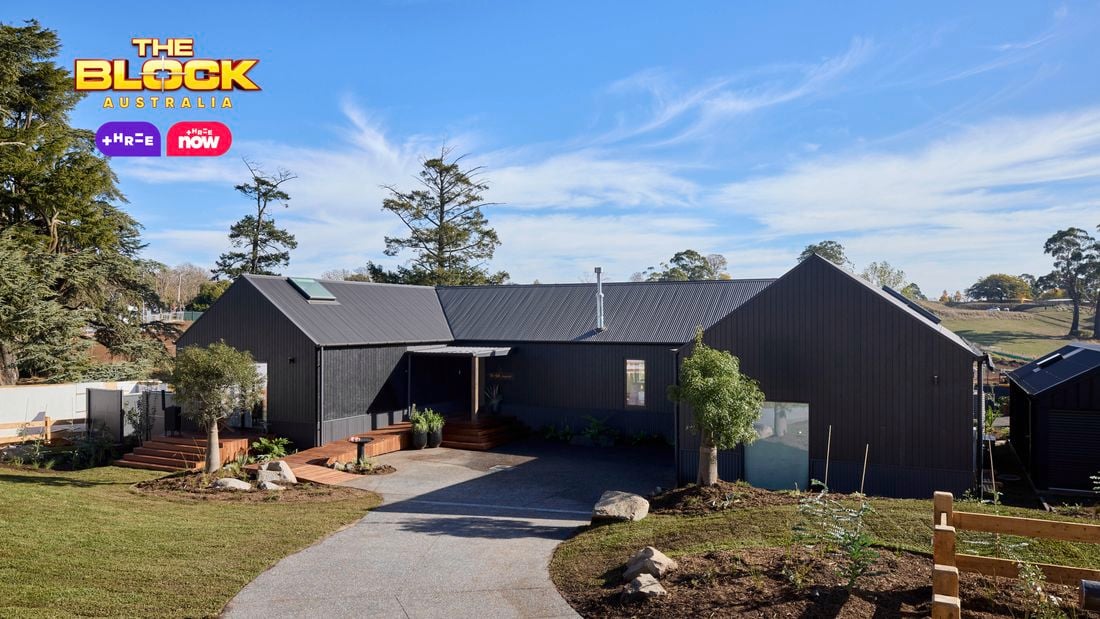 The front of a house with a driveway in it, trees, and a timber fence.