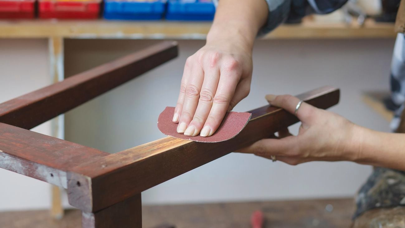 Woman restoring timber furniture using sandpaper.