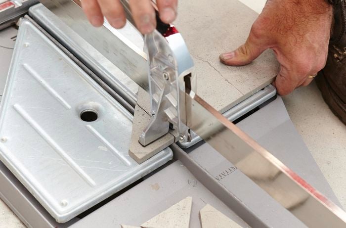 A person using a tile cutter to cut a tile
