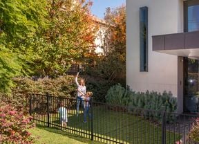 Black flat top fencing at the front of a modern house with a woman and children playing a game.