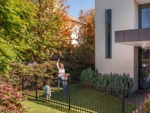Black flat top fencing at the front of a modern house with a woman and children playing a game.
