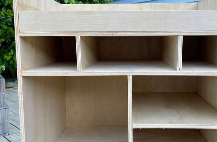 A DIY camp kitchen box on a deck outside with panels of wood attached to create shelves and a lid.