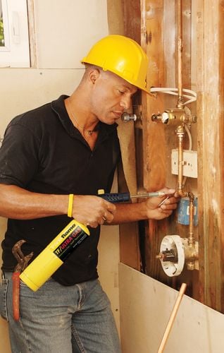 A tradesman mending some copper pipes with a handheld welding torch