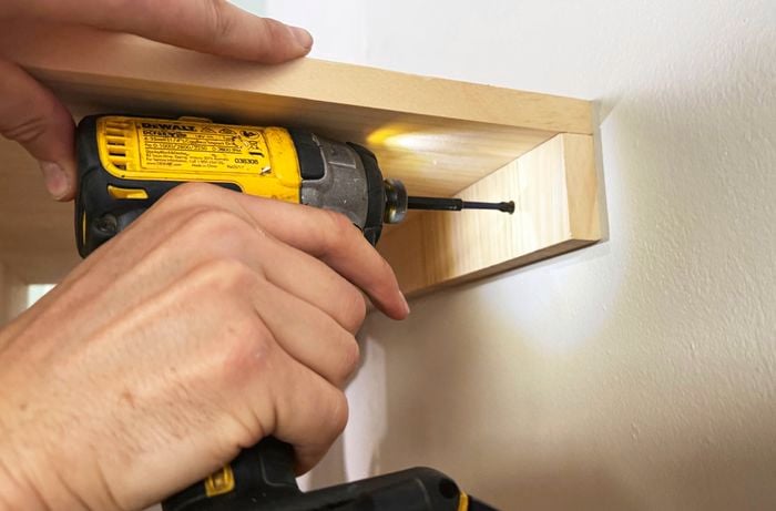 Close up of a drill driving a screw into a timber frame on a wall.