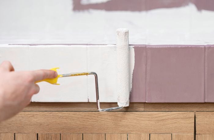 A person is painting over tiles with white paint using a small paint roller.