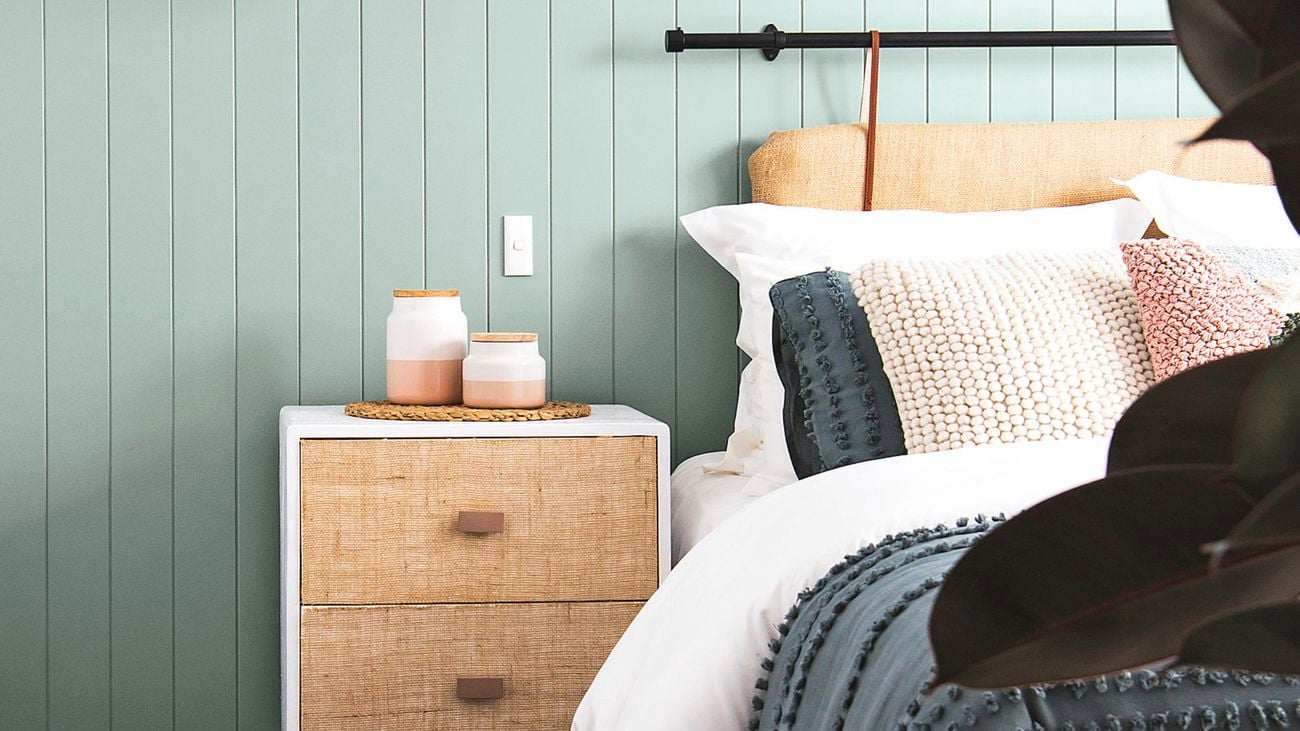 Green weatherboards in a bedroom interior with bed, cushions and side table.