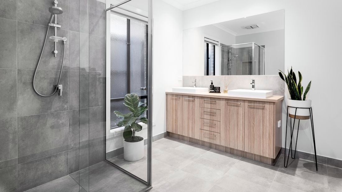 Modern bathroom with grey stone shower walls, timber benchtop, white sink and toilet, and big mirror on the wall.