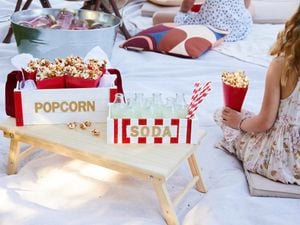 Soda and popcorn tray sitting on a bed tray while in a picnic style movie night is happening