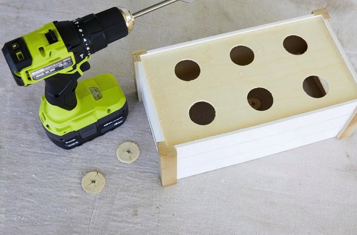 A wooden crate with holes in the bottom of it. A cordless drill sits next to it.