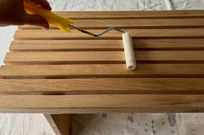A hand using a roller to varnish the table.