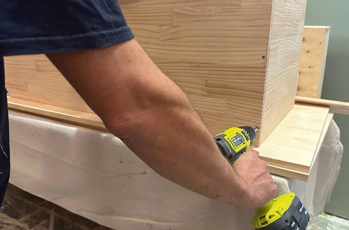 A hand using a drill to join the timber panels to make the bench seat