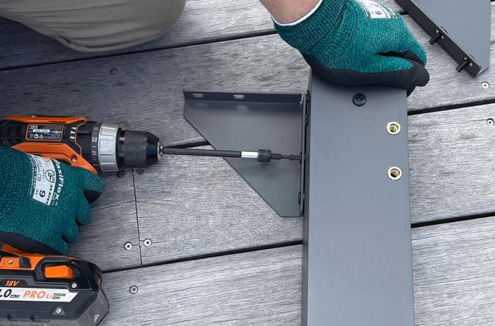Person attaching corner brace to the post of a gazebo with a drill.