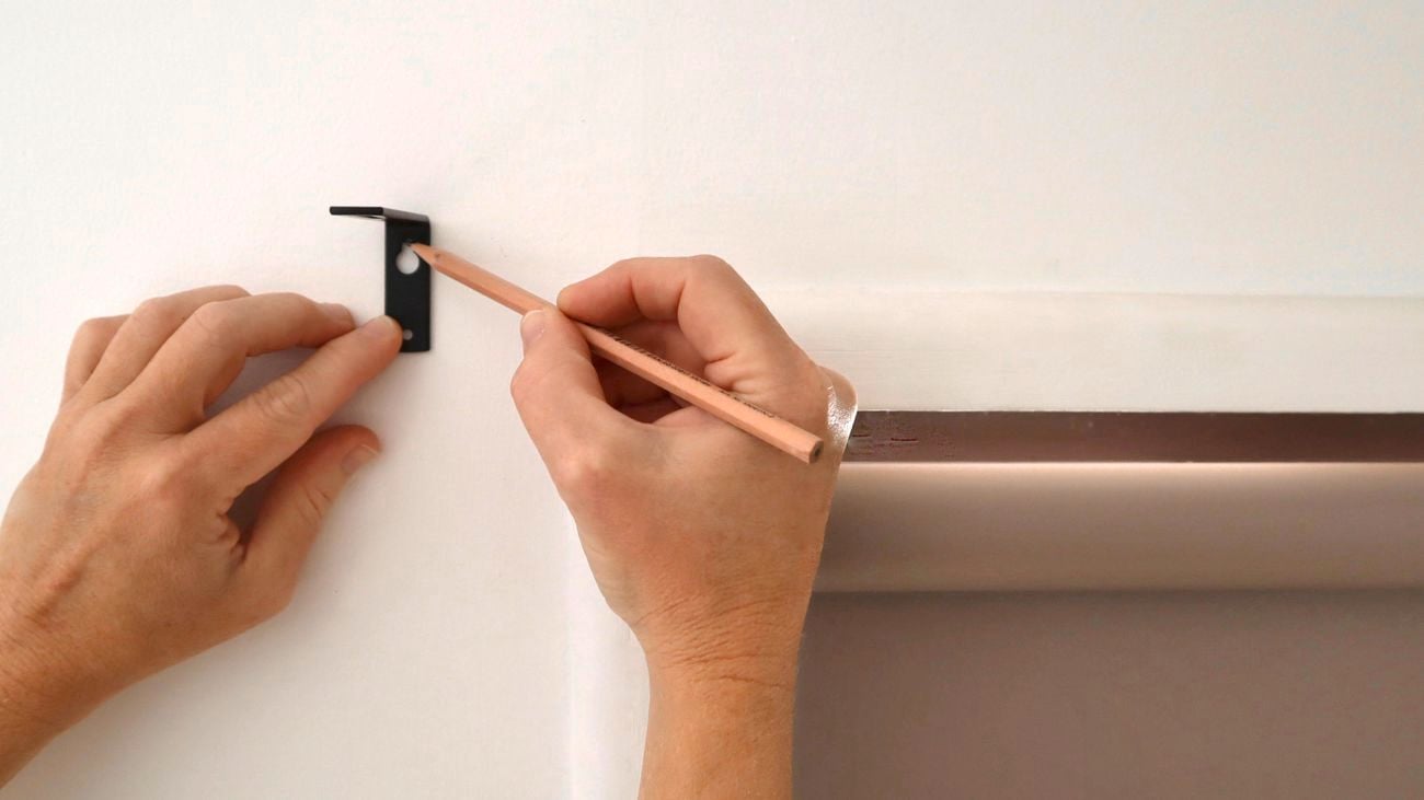 A person marking the position for a curtain rail bracket on a wall.