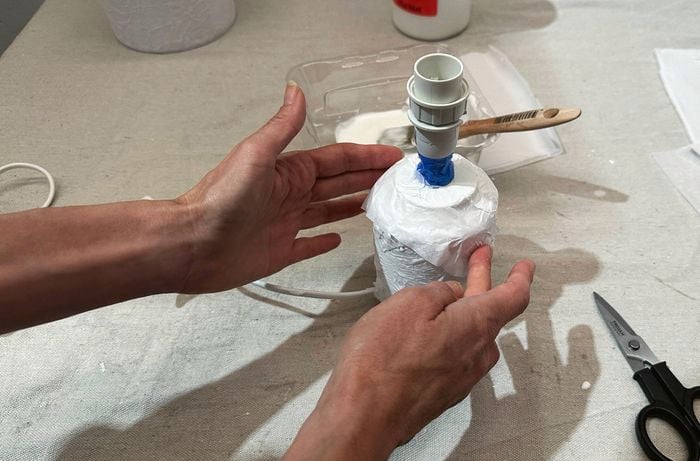 An overhead shot of two hands pushing down tissue paper, paper mache style, onto the base of a lamp shade