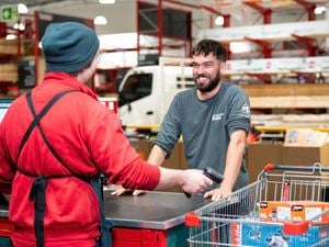 A man in a Bunnings Trade long-sleeved shirt smiles at a Bunnings Warehouse team member, who is scanning products in his trollery.