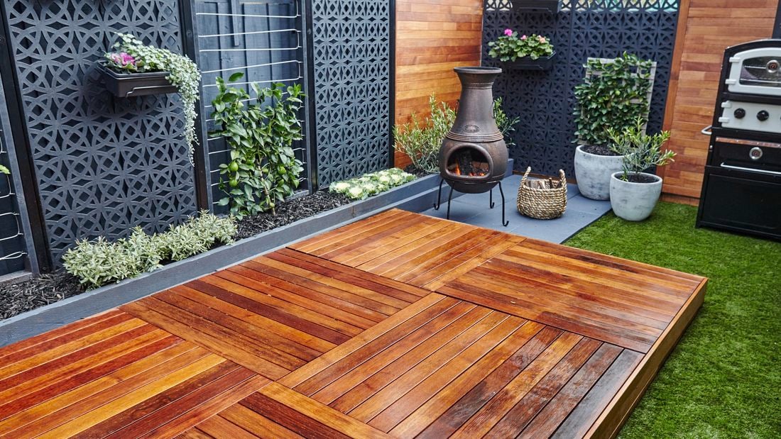A welcoming wooden patio space with outside fire, wood, BBQ and potted plants.