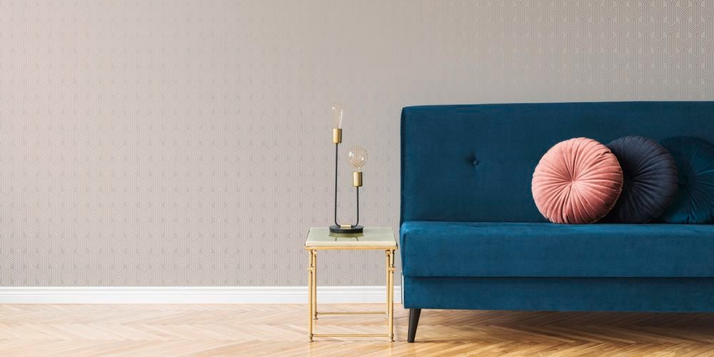 Dark blue couch with round decorative cushions, side table with lamp and neutral patterned wallpaper.