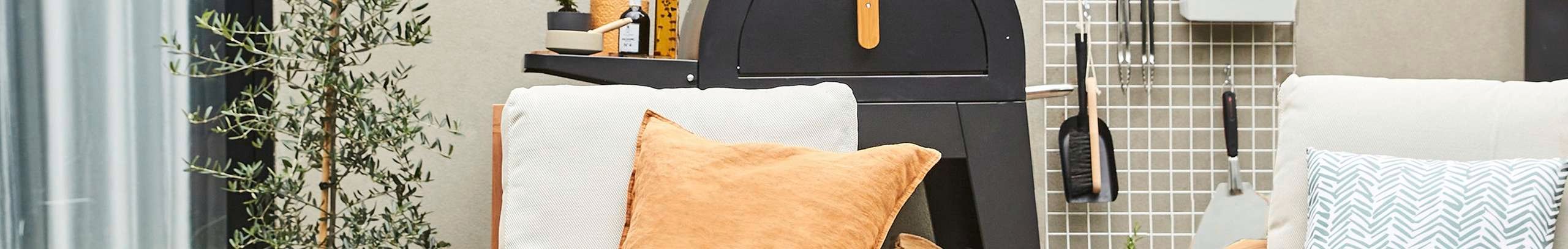 timber outdoor lounge chairs with cushions next to side table with drinks, pizza oven and olive tree