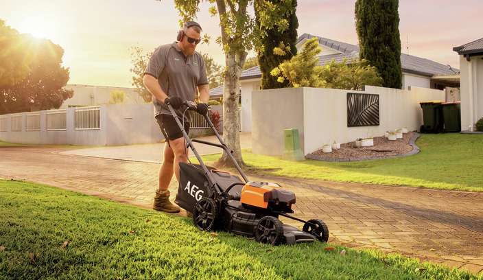 Person mowing a lawn in a well-maintained suburban garden during golden-hour light.