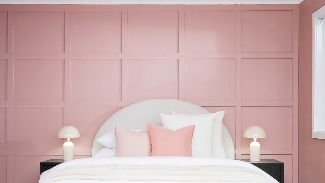 A finished bedroom featuring a pink batten feature wall behind a neatly made bed and matching bedside lamps.