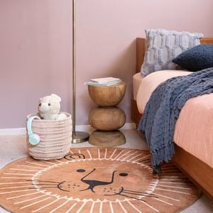 A kids bedroom with a bed, rug, cane basket and light stand in it.
