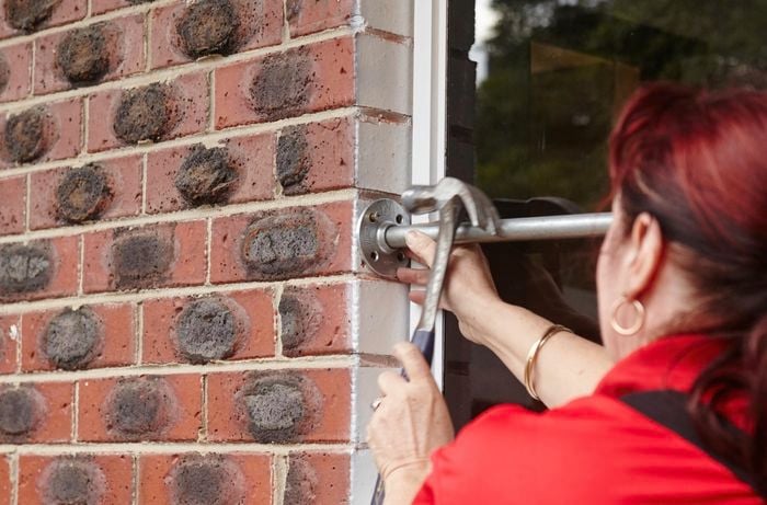 A person using a hammer to tap a screw securing a flange and pipe to a wall