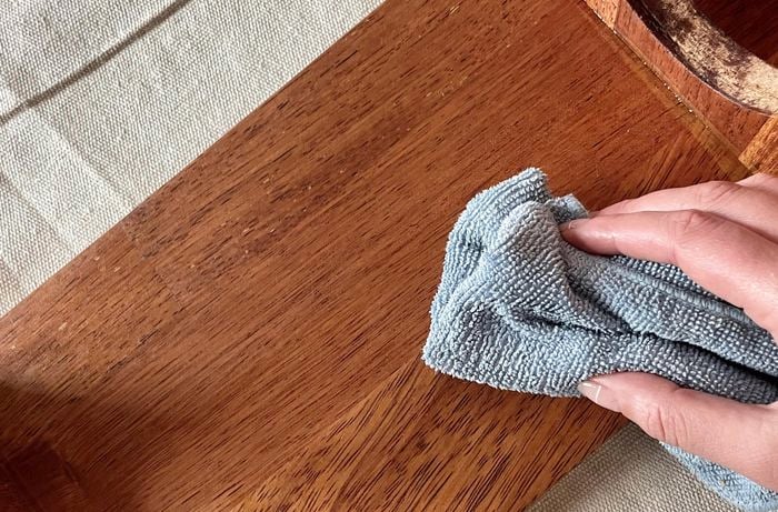 Hand uses cloth to clean plank of wood