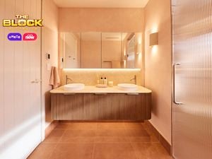 Modern bathroom with double round sinks, chrome faucets, mirrored cabinets, soft pink walls, and toiletries on the vanity. 