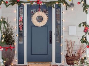 A festive front door decorated with a wreath, garland, ornaments, and Christmas lights.