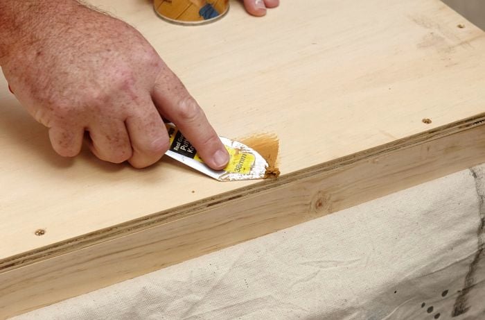 A person filling a hole in plywood using wood filler