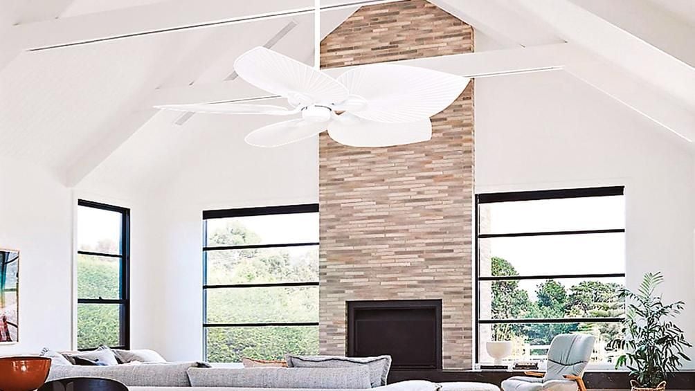 A modern living room featuring a timber dining table, grey lounge, cream brick fire place and a white ceiling fan.