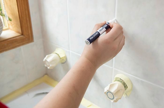 A grout pen being used to clean grout between bathroom tiles
