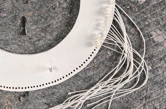 White cord threaded through a circle plywood frame