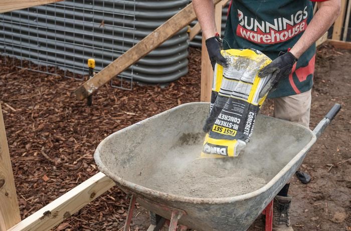 A Bunnings Team Member pouring concrete mix into a wheelbarrow
