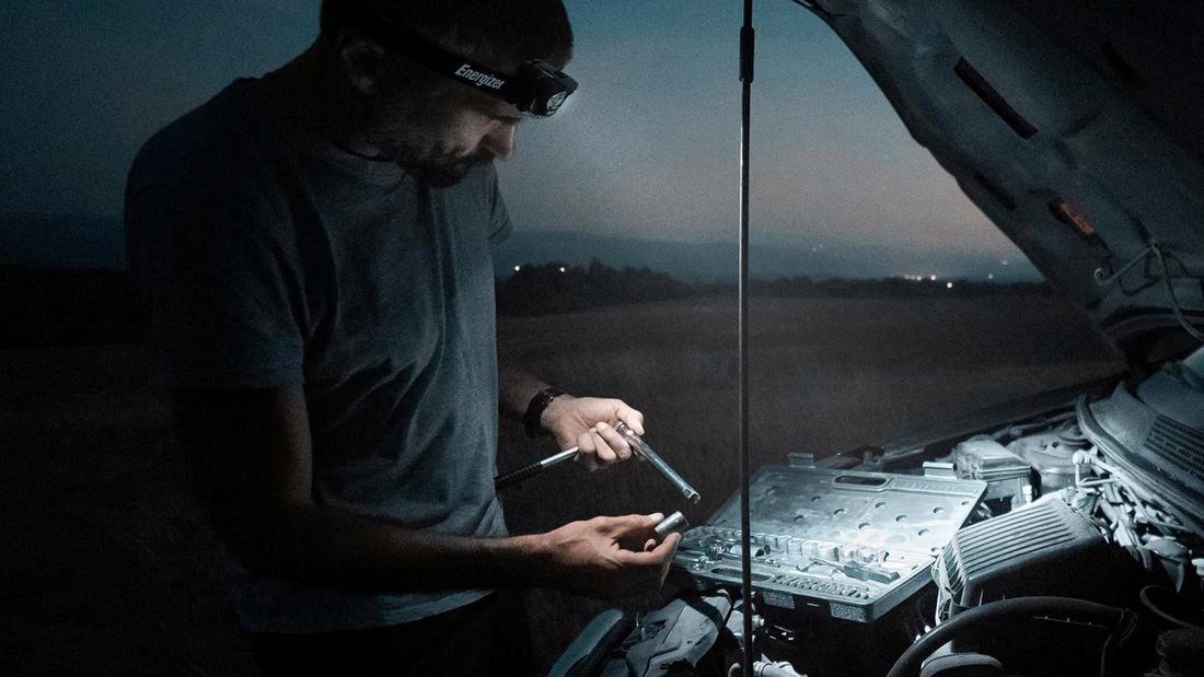 Man using light to fix car engine in dark 