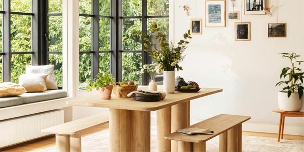 Indoor dining area with a timber dining table and chairs, wall prints and windows.