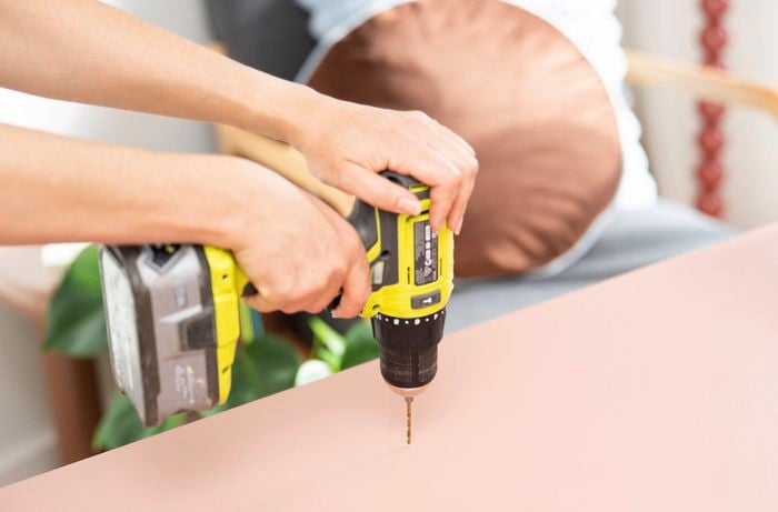 Using a cordless drill to attach a shelf to a painted wall panel during a DIY bookshelf project.