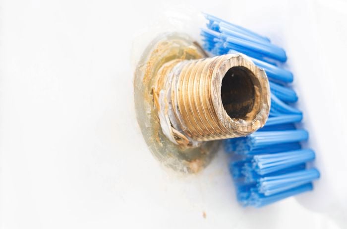 A person is cleaning old plumber's tape and residue from shower arm threads before installing a new shower head