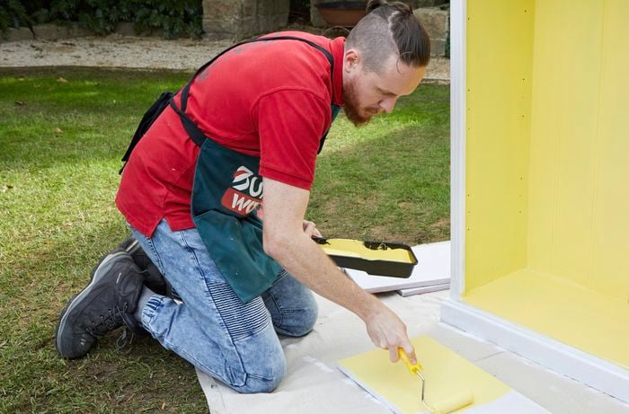 A man paints a bright yellow paint colour onto a bookcase.