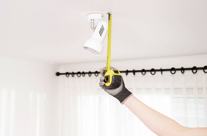 A person is measuring the height of a pendant light fitting to ensure the woven basket shade will fit neatly and provide the correct clearance. 