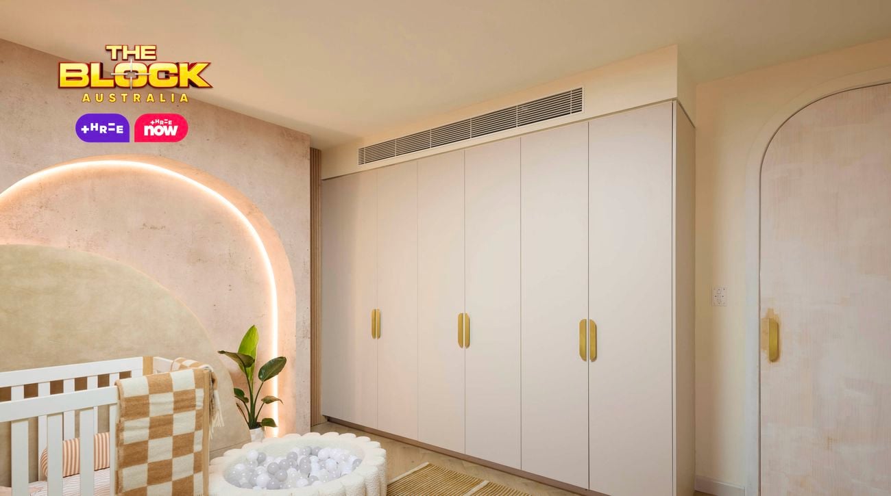 Neutral baby bedroom with brown and tan colours. Showcasing a cot and small ball pit in front of an arched feature wall with feature lighting. There is a wardrobe on the opposite wall.