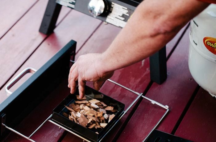 Person adding wood chips to a vertical smoker tray