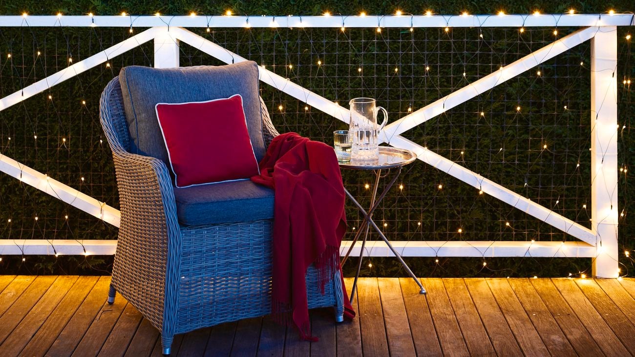 Fairy lights along a balcony in an outdoor room at night, with a comfortable chair