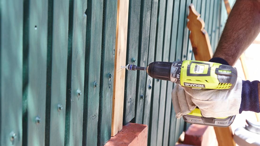 Person drilling pickets in picket fence.
