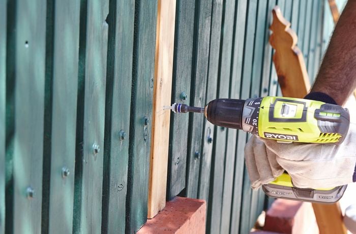 Person drilling pickets in picket fence.