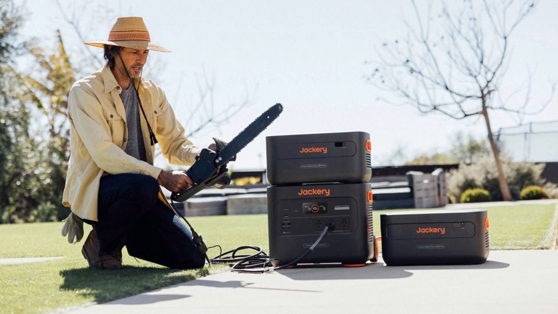 A man on the ground with a chainsaw, a Jackery solar generator and battery system beside him
