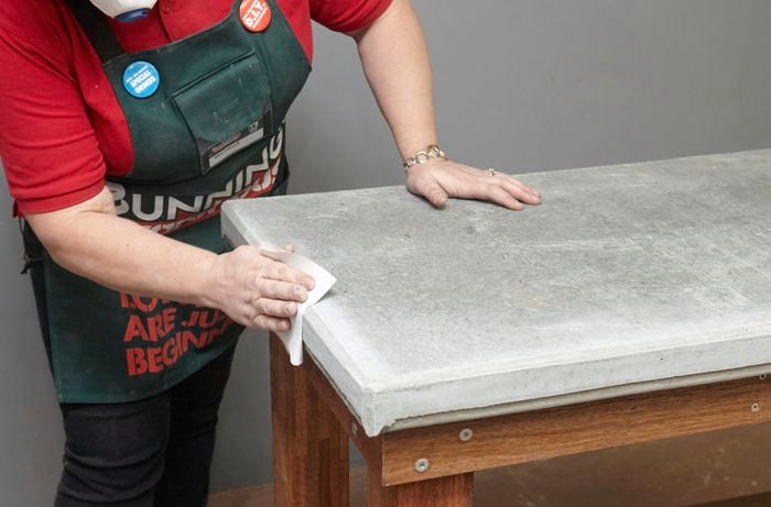 Person wiping concrete table benchtop with cloth.