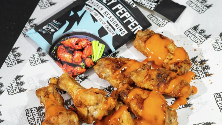 Grilled chicken wings topped with spicy sauce, served alongside a honey pepper seasoning packet.