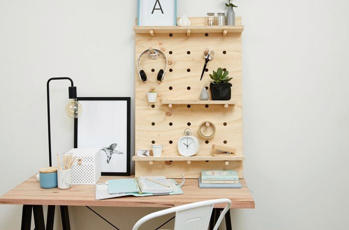 A pegboard shelf of plywood and dowel holding headphones and other objects